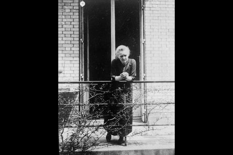 A black and white photo of Marie Curie leaning over the rails of a balcony